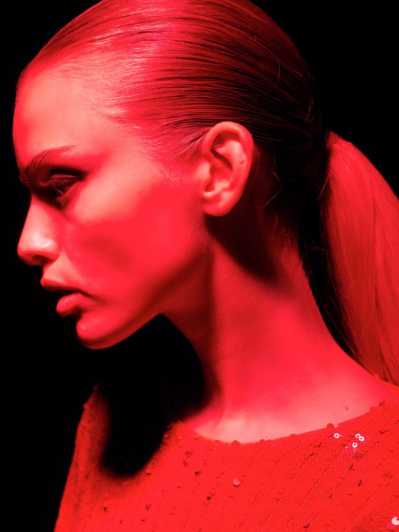 Profile shot of a woman with fair skin, wearing a red top, in a dark studio with a red lighting scheme and a low-key exposure.
