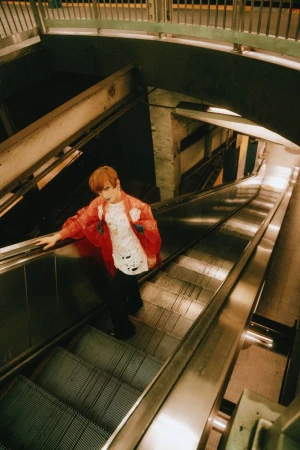 Adult female with short red hair and red jacket descending subway escalator with grey handrails and stairs. Subway station interior.