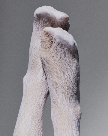 Close-up shot of two legs crossed wearing patterned white stockings, against a grey backdrop in an indoor setting. Fashion.