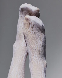 Close-up of feet wearing white lace socks against a neutral grey studio background for Scensored Afterglow.