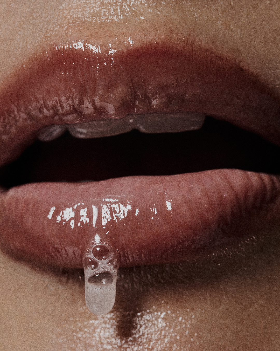 Close-up shot of a woman's glossy lips with liquid dripping, highlighting beauty and skincare.