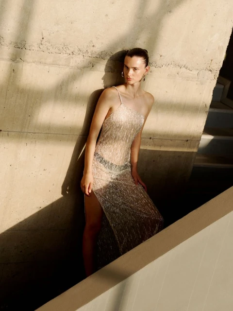 Fashion shot of a woman in a light tan dress posing on a set of concrete stairs with sunlight casting shadows on the concrete.