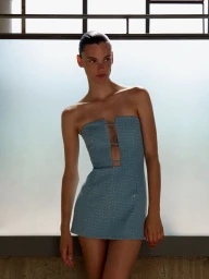 Model Sara Dijkink wearing a strapless blue textured minidress by ILA against a light-filled window backdrop.