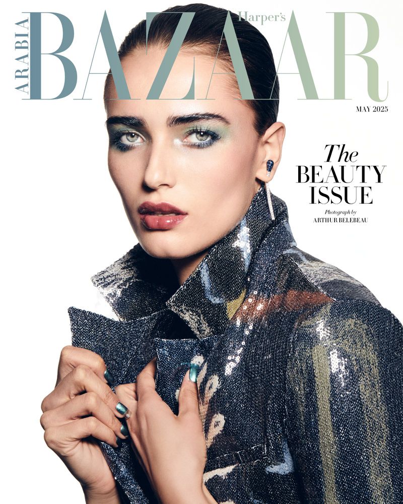 A female model with dramatic green eyeshadow and a sequined jacket poses against a white studio background.