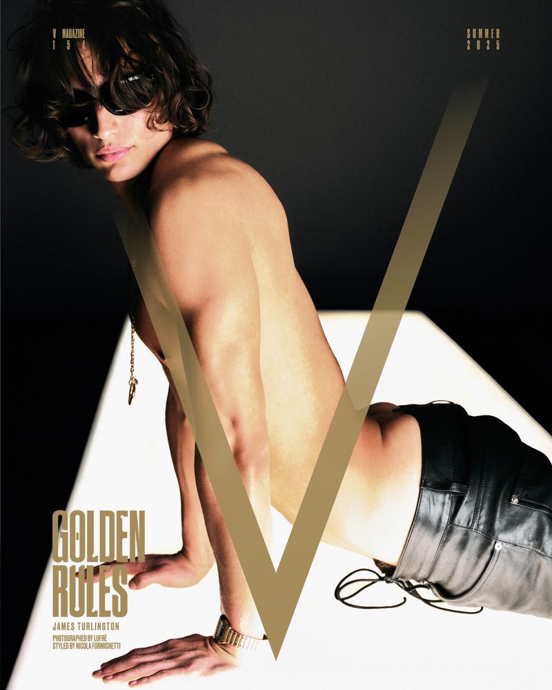 Shirtless man with sunglasses poses with V Magazine, showcasing his gold watch and necklace against a spotlighted backdrop.