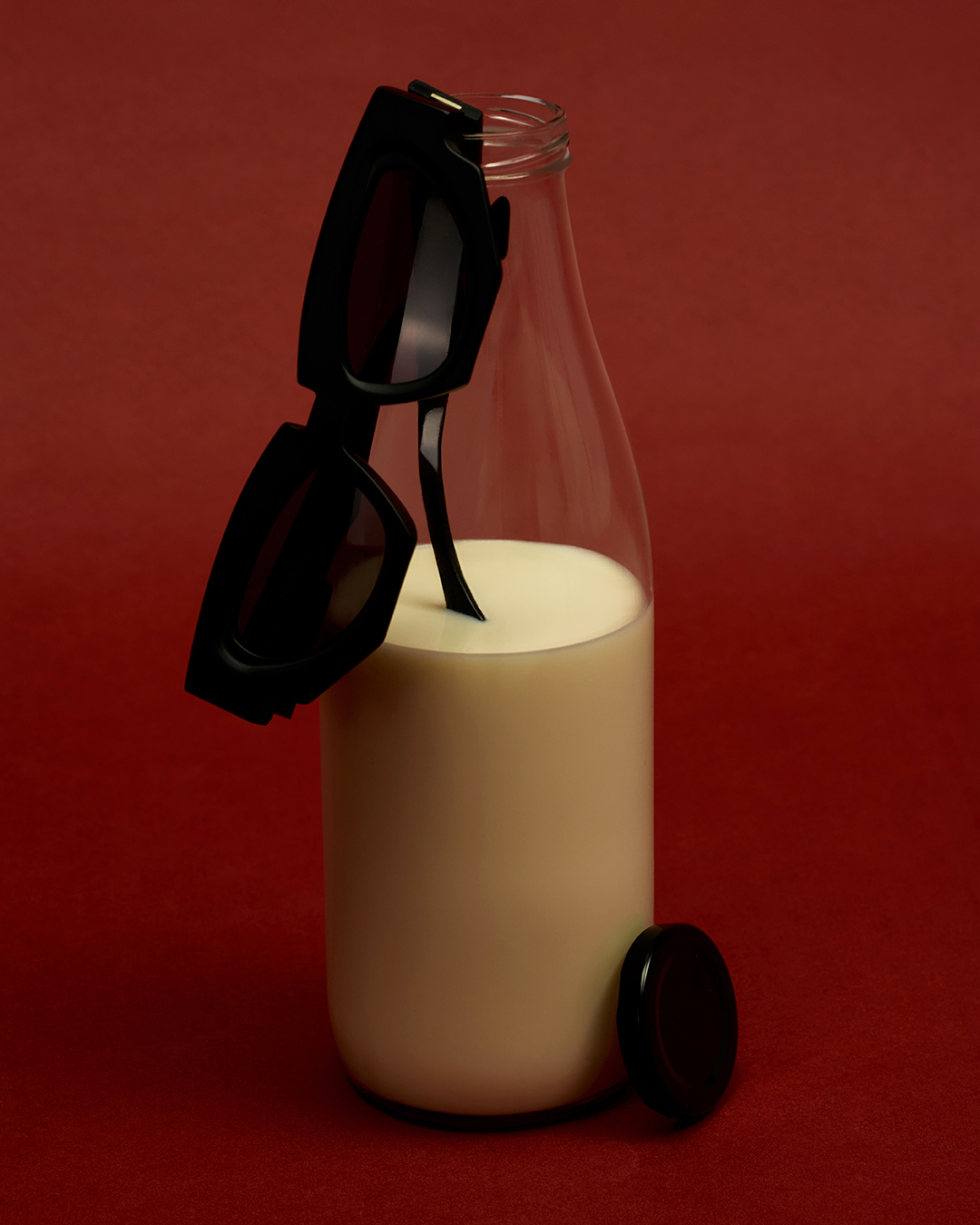 Sunglasses on a milk bottle set against a red background creating a minimalist and visually striking composition for fashion or food.