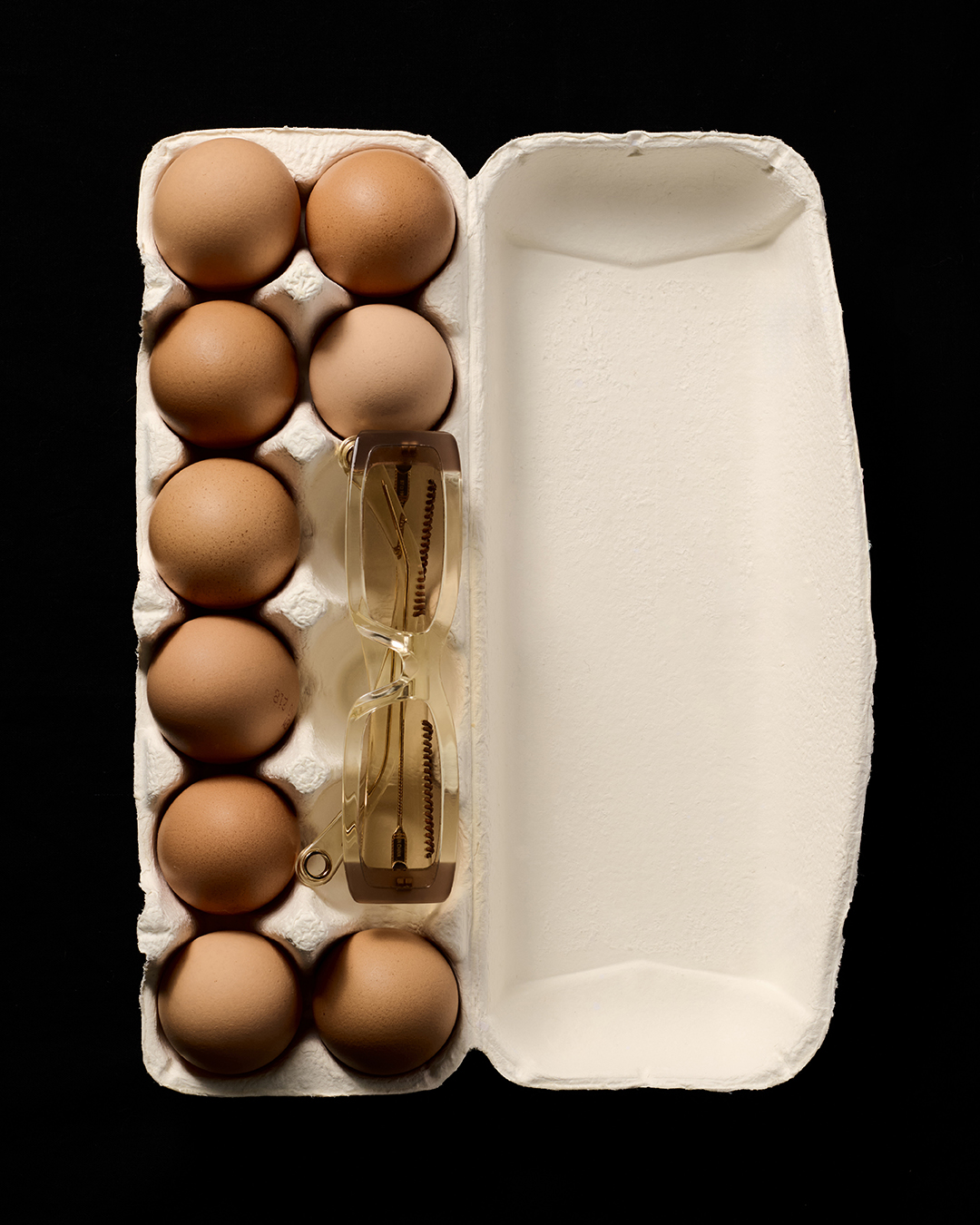 Overhead shot of a carton of eggs with an hourglass inside, studio lighting, black background.