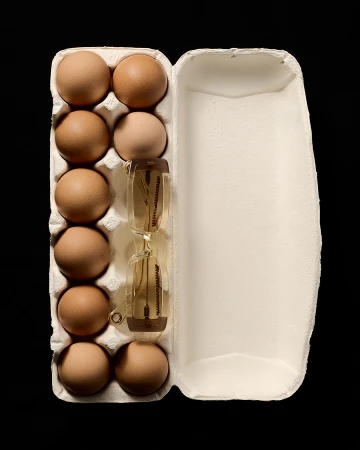 Overhead shot of a carton of eggs with an hourglass inside, studio lighting, black background.