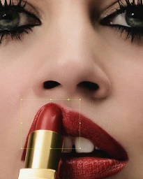 Extreme close-up portrait of a woman applying red lipstick with dramatic black eyeliner and heavy mascara.