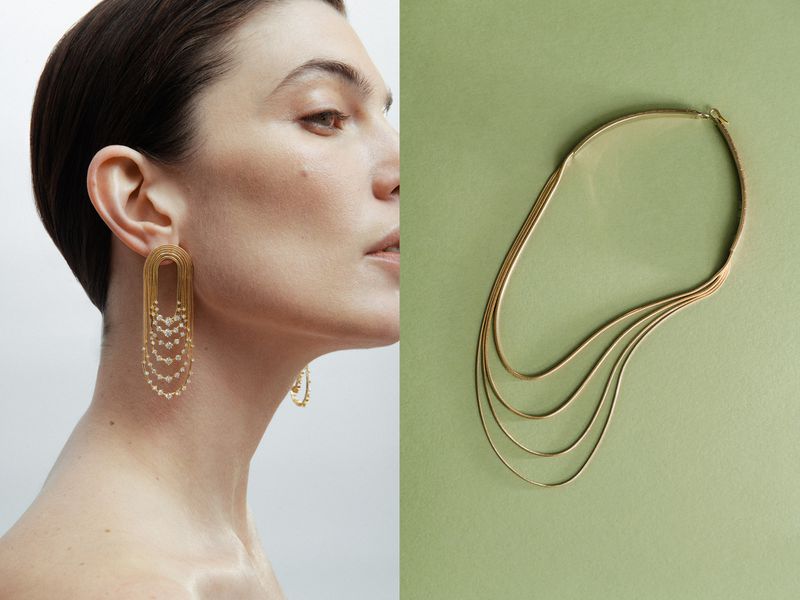 Model wearing gold statement earrings with a matching gold layered necklace, shot in a photo studio against a neutral background.