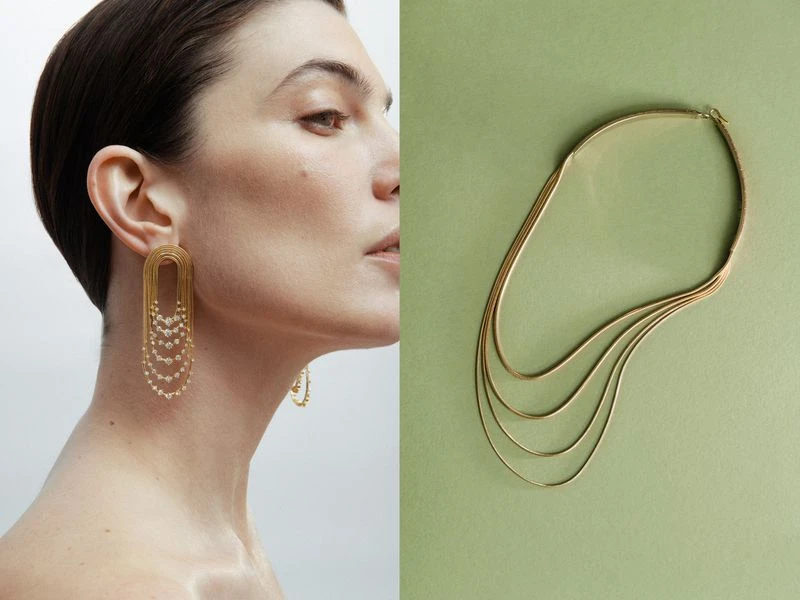 Model wearing gold statement earrings with a matching gold layered necklace, shot in a photo studio against a neutral background.