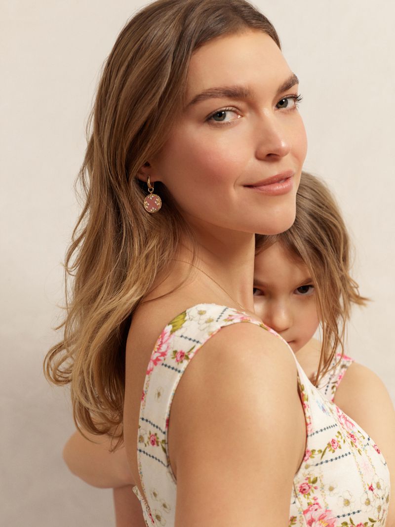 Woman and child in floral dresses embrace in a close-up studio portrait. The woman wears gold earrings, and the child looks towards the camera.