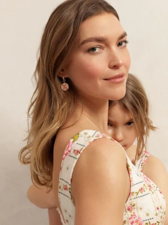 Woman and child in floral dresses embrace in a close-up studio portrait. The woman wears gold earrings, and the child looks towards the camera.