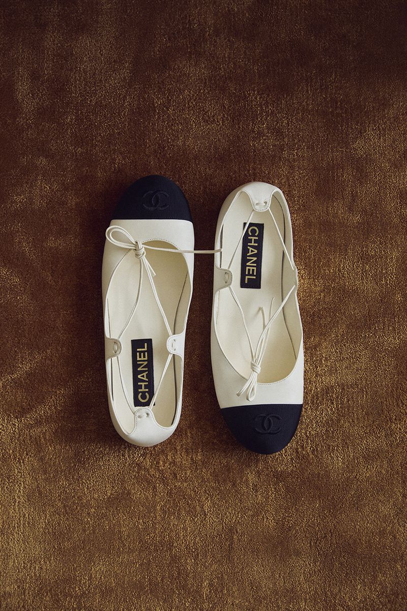 Two Chanel ballet flats are displayed on a textured brown surface in a studio setting, showcasing high-fashion elegance.