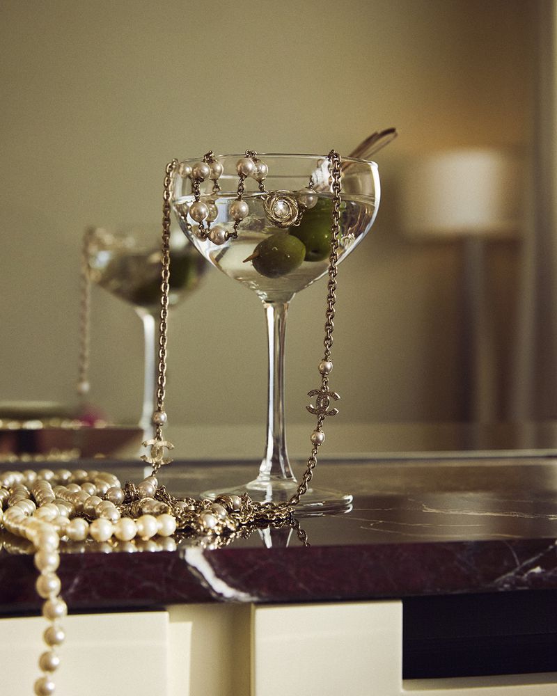 Close-up still life of cocktail glasses filled with martinis and garnished with olives, accessorized with pearl and chain necklaces.