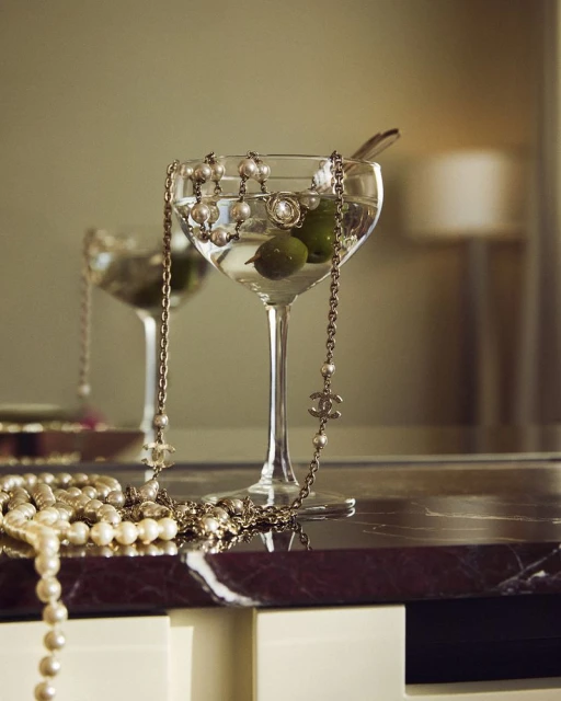 Close-up still life of cocktail glasses filled with martinis and garnished with olives, accessorized with pearl and chain necklaces.