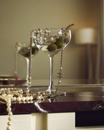 Close-up still life of cocktail glasses filled with martinis and garnished with olives, accessorized with pearl and chain necklaces.