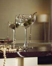 A cocktail glass containing two olives and draped with pearl necklaces sitting on a dark marble surface.
