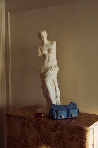 Blue quilted handbag resting on a burl wood cabinet next to a classic white sculpture against a warm neutral wall