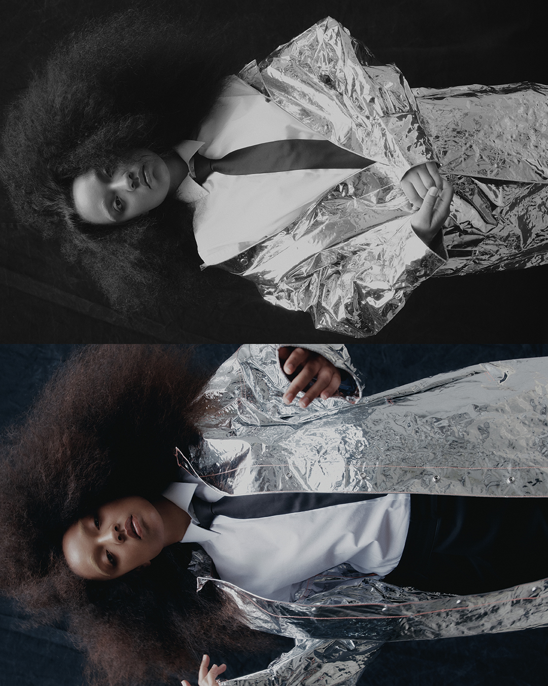A black model with an afro lies down wearing a white shirt, black tie and black pants, and is covered in a shiny silver blanket.