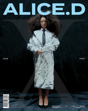 Magazine cover featuring a woman with voluminous hair in a metallic silver coat, black tie, and heels against a black background.