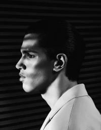 Monochrome portrait in profile of a male model with slicked-back hair wearing a collared shirt against a striped background