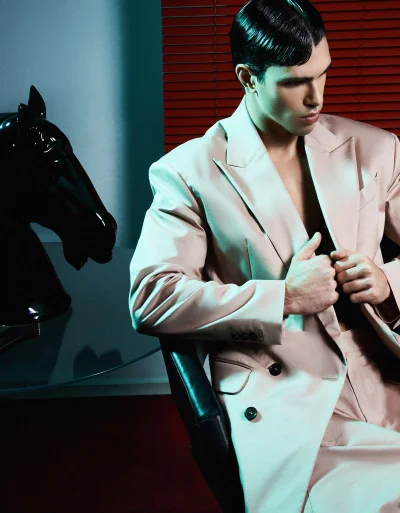Man wearing a light suit jacket seated next to a black horse statue against red blinds