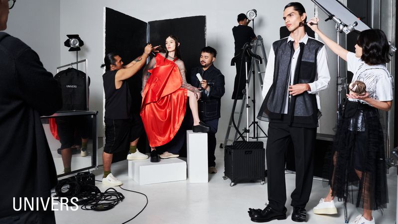 Fashion photo shoot in a studio, featuring models in stylish outfits getting touch-ups by makeup artists under bright studio lighting.