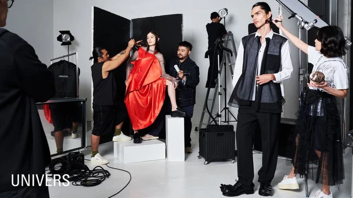 Behind-the-scenes fashion photo showing a crew styling models on a white studio set for UNIVERS SS25.