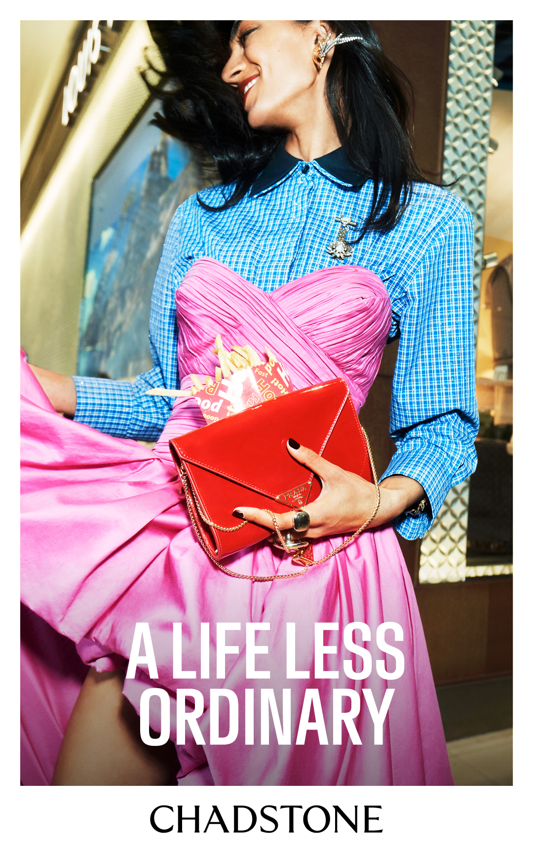 Fashionable woman in a pink dress and blue shirt holds a red purse in a retail environment, showcasing a modern and stylish aesthetic.