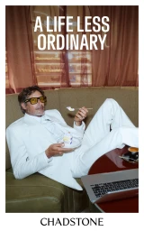 Man wearing a white suit and yellow sunglasses reclining on a green sofa while eating cake, for Chadstone brand campaign.
