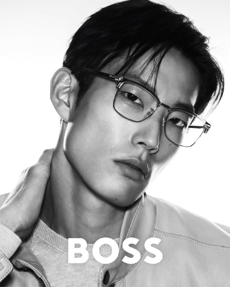 Close-up black and white studio portrait of an Asian male model wearing glasses and a light jacket for a fashion advertisement.