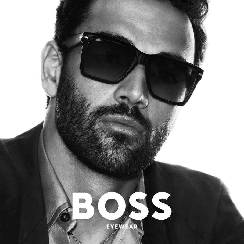 A striking black and white studio shot of a bearded man wearing sunglasses, showcasing the BOSS eyewear collection.