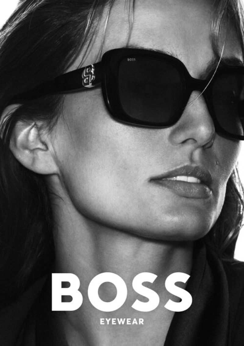 Close-up of an adult woman with dark hair, wearing oversized black sunglasses, set against a bright backdrop with a 'BOSS EYEWEAR' logo.