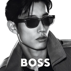 Close-up portrait of a male model wearing dark sunglasses and a collared jacket against a white background for BOSS 2025 eyewear campaign