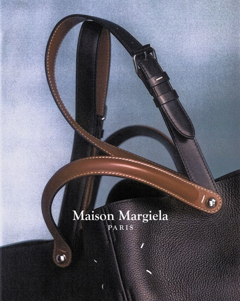 Close-up shot of a black leather Maison Margiela tote bag with dual handles, against a soft blue background, showcasing fashion.
