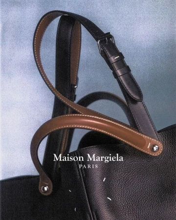 Close-up shot of a black leather Maison Margiela tote bag with dual handles, against a soft blue background, showcasing fashion.