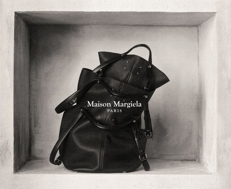 Maison Margiela black leather handbag is showcased in a recessed, wall-like space with a stark, minimalist presentation.