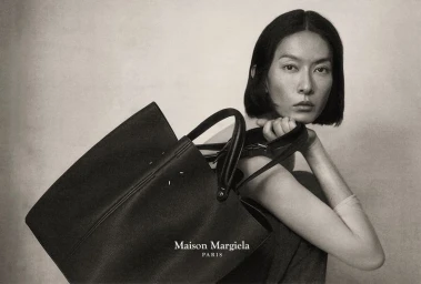 Model with dark bob hairstyle holding a large black tote bag against a neutral studio background