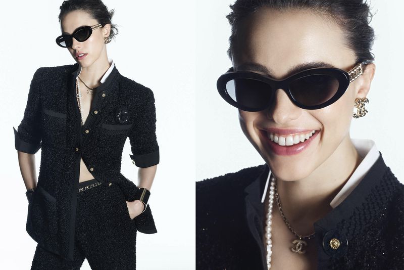 Fashion shot of a woman in a black tweed suit and sunglasses, smiling, with Chanel jewelry, against a bright white backdrop.