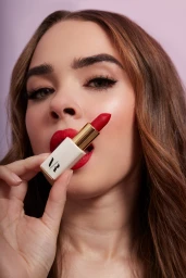 Close-up portrait of a woman holding a red lipstick near her lips for VR Face and Body rebrand imagery