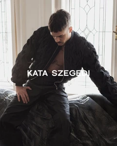 Model in textured black bomber jacket posing indoors against a patterned glass door for Kata Szegedi FW2526 campaign.