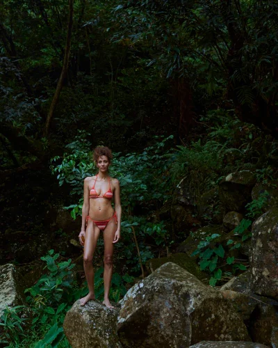 Model standing on a mossy rock in a dense tropical forest wearing an orange bikini for One&Only