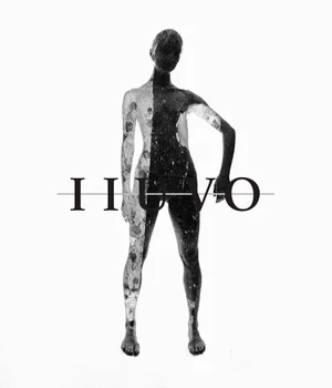 Monochrome vertical portrait of a figure covered in splattered black and white paint standing against a bright white background with IIUVO text