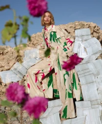 Model in printed coat against rocky background with pink flowers in foreground