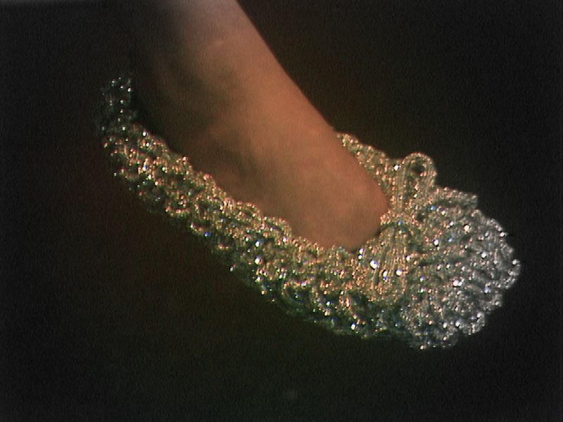 Close-up of a foot wearing a silver, sparkly, decorative slipper against a dark background. Elegant footwear for special occasions.