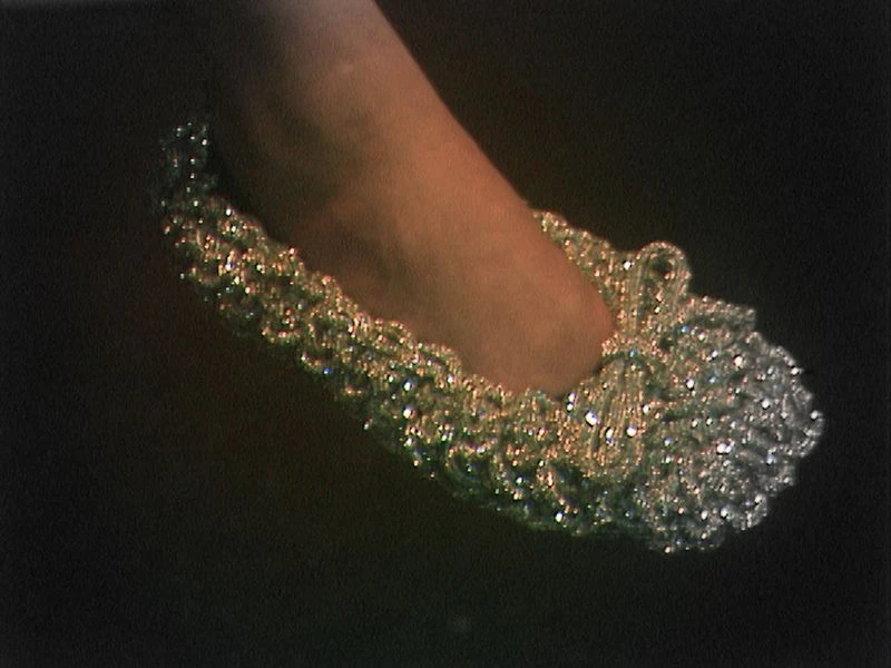 Close-up of a foot wearing a silver, sparkly, decorative slipper against a dark background. Elegant footwear for special occasions.