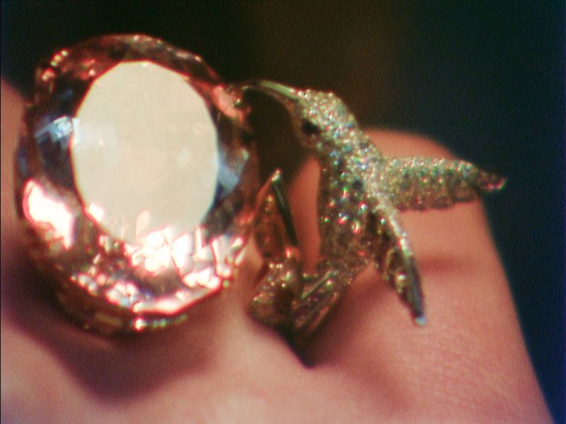 Close-up of a sparkling bird-shaped ring with a large gemstone, set against a dark backdrop. Jewelry design with intricate details.