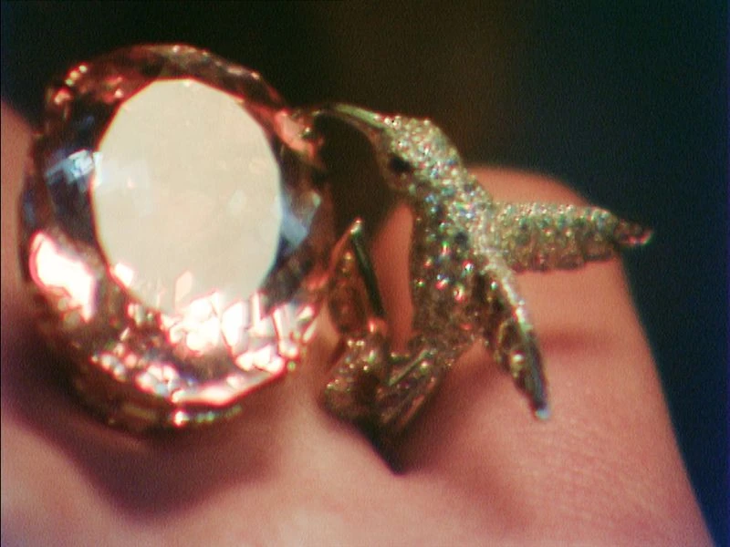 Close-up of a sparkling bird-shaped ring with a large gemstone, set against a dark backdrop. Jewelry design with intricate details.