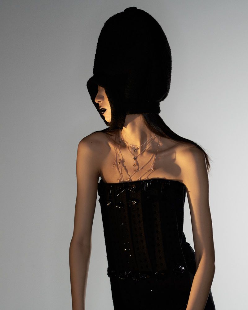Fashion portrait of a slender adult woman in a black strapless dress and large bonnet against a gradient grey background in studio lighting.